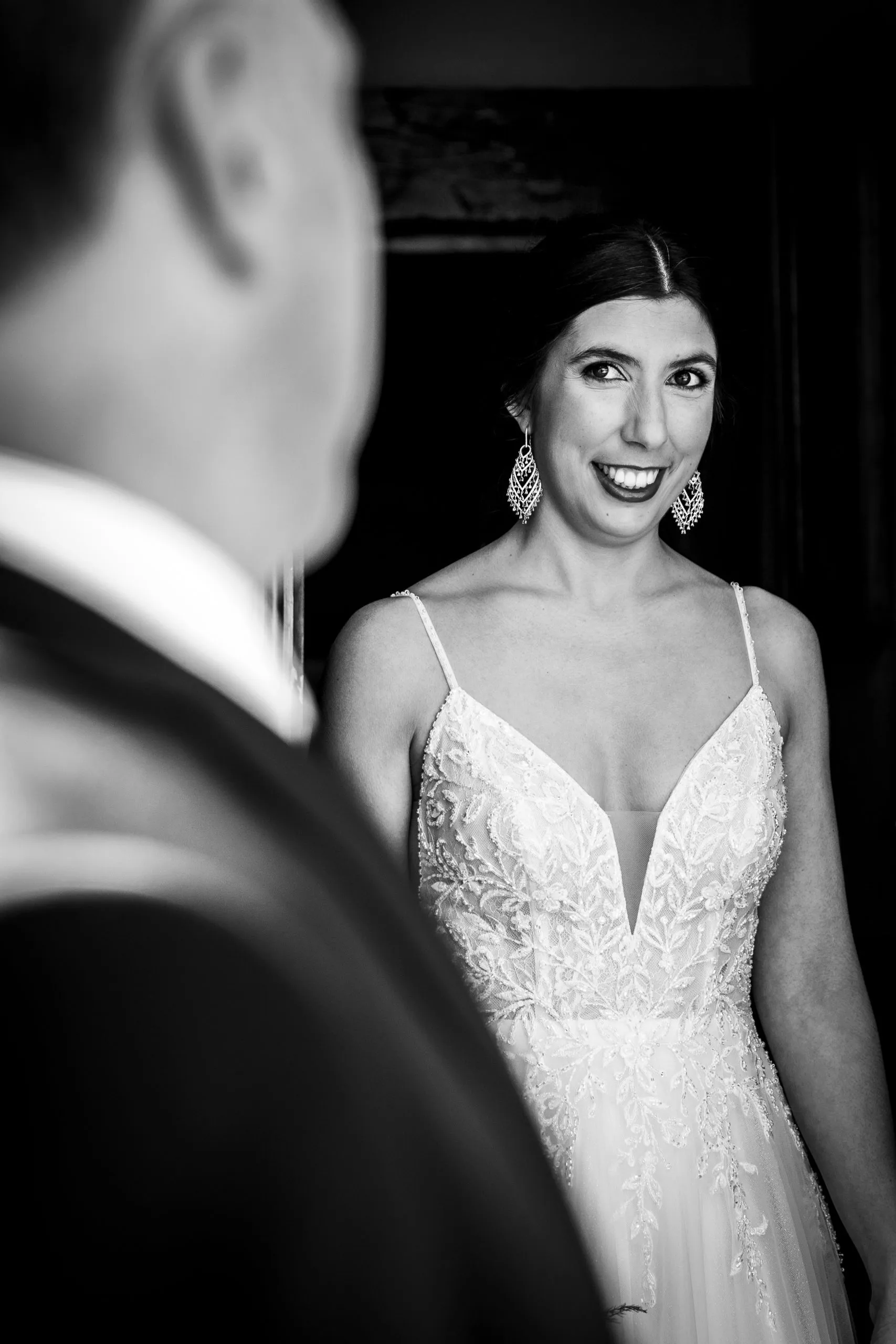 Novia sonriendo en blanco y negro, con el novio desenfocado en primer plano