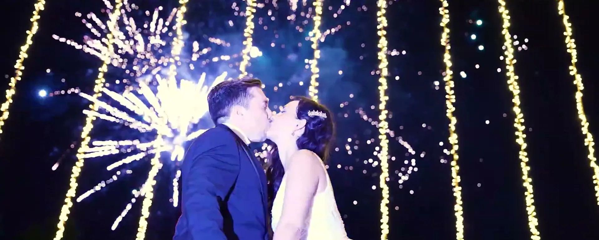 Couple kissing under fireworks and strings of lights