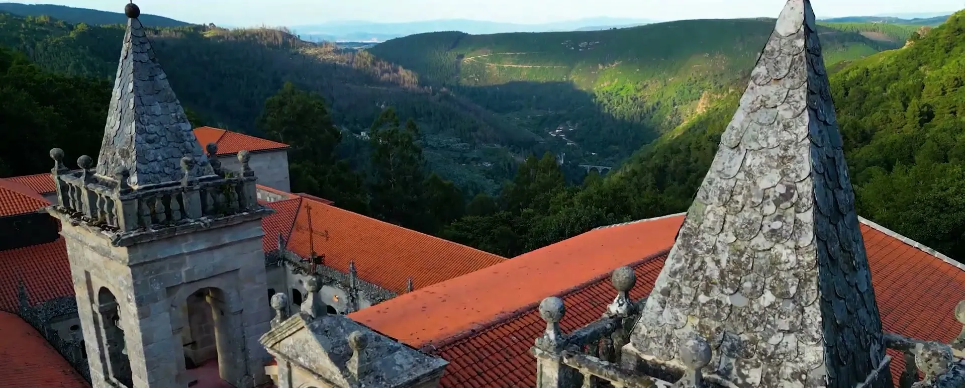 Aerial view of stone towers and tiled roofs above green hills
