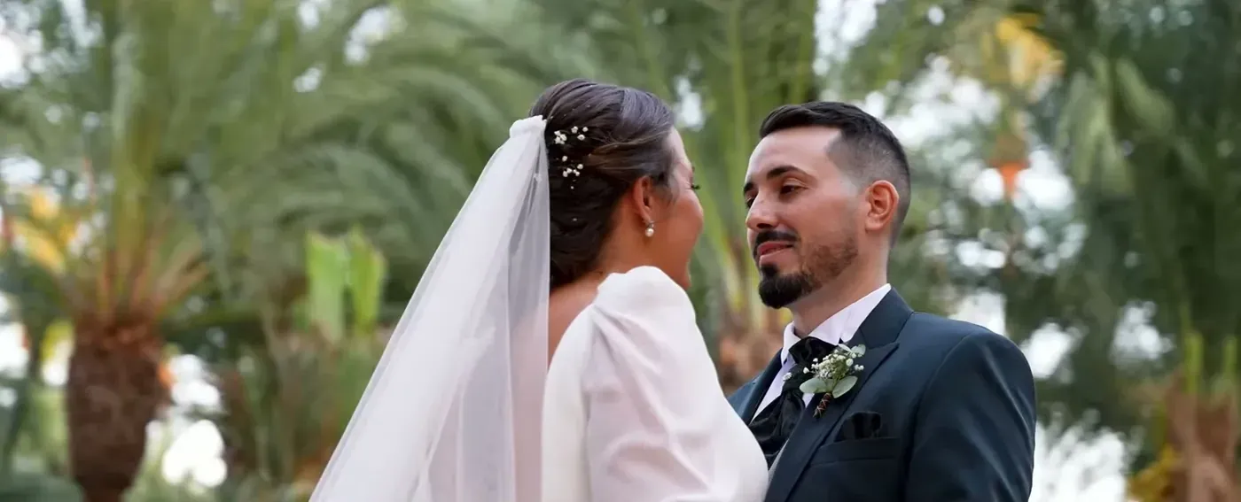 Bride with a long veil smiling at the groom under palm trees