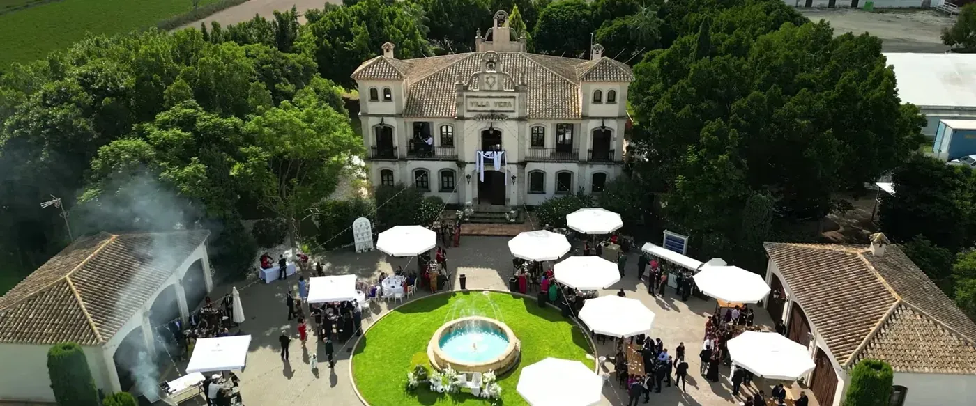 Aerial view of a palace-style finca with white umbrellas and a fountain in the garden