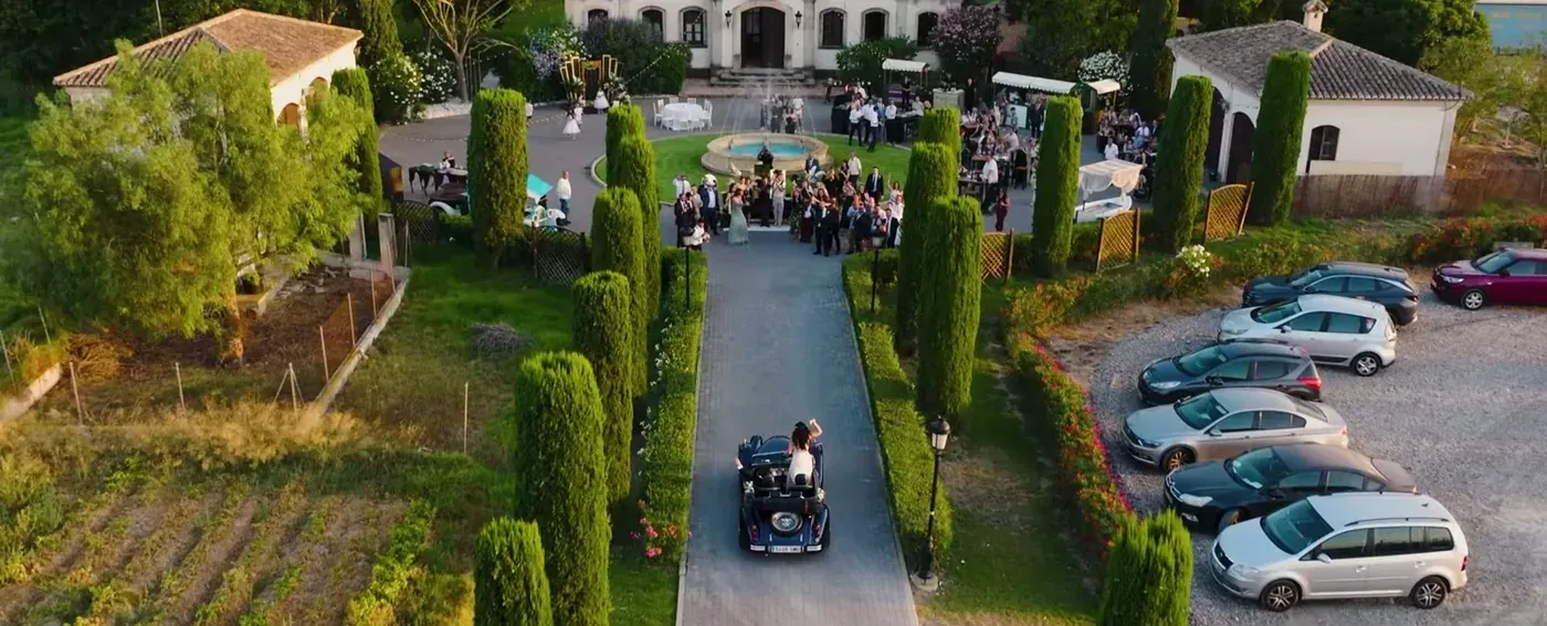 Aerial view of a vintage car arriving at a finca as guests wait outside
