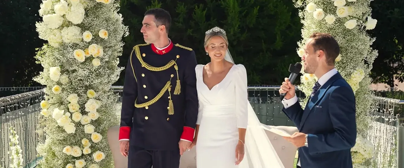 The couple and their officiant at a flower-covered altar during an outdoor ceremony