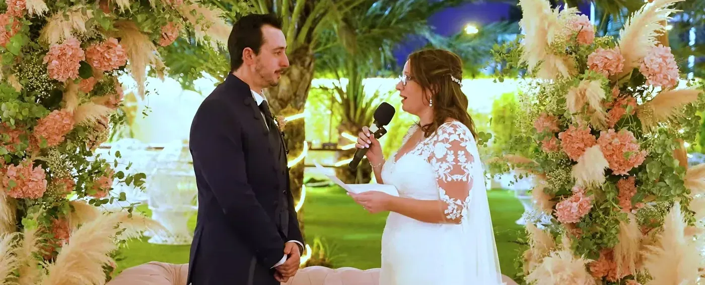 Bride reading her vows under a floral arch at night